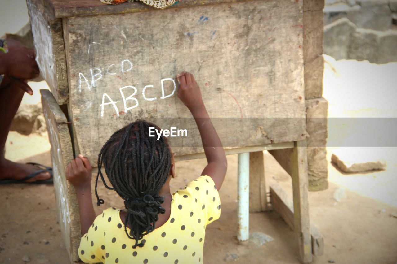 High angle rear view of girl writing alphabets with chalk on wood