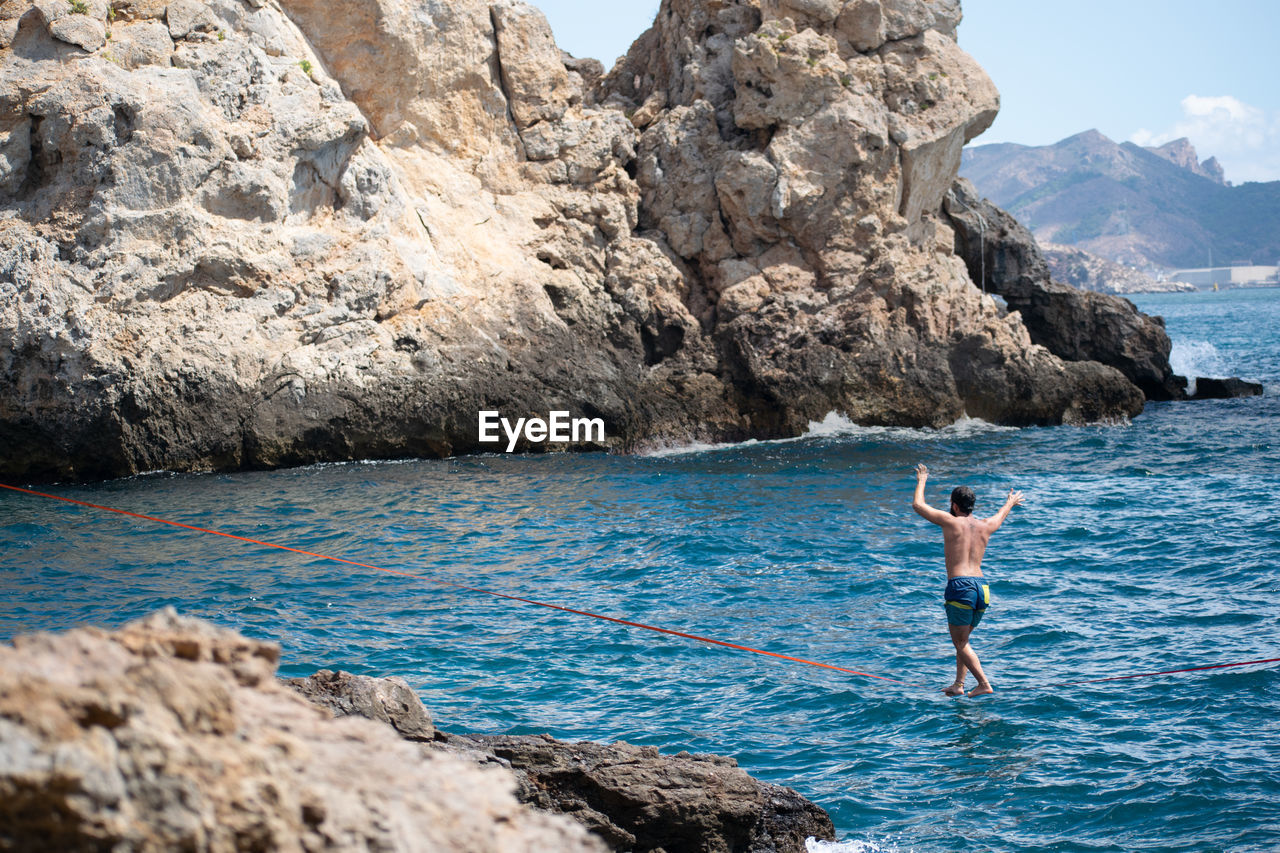 FULL LENGTH OF SHIRTLESS MAN STANDING ON ROCKS