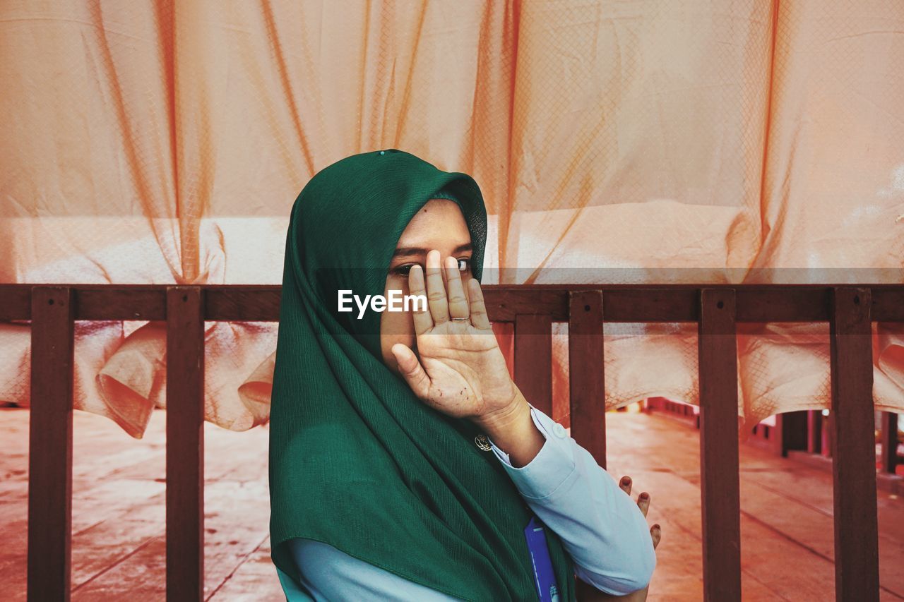 Portrait of woman showing stop gesture while standing against orange curtain