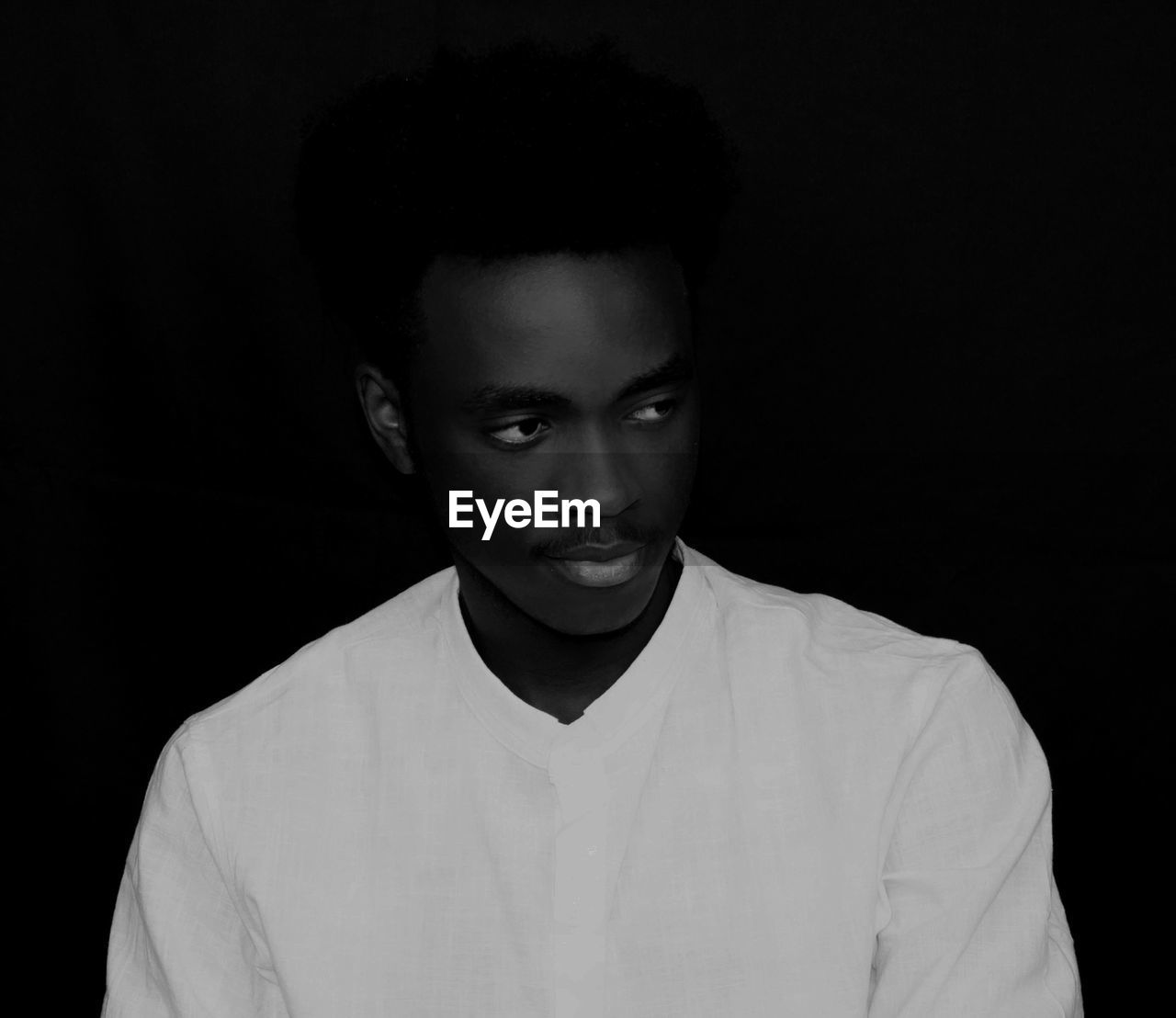 Young man looking away while standing against black background