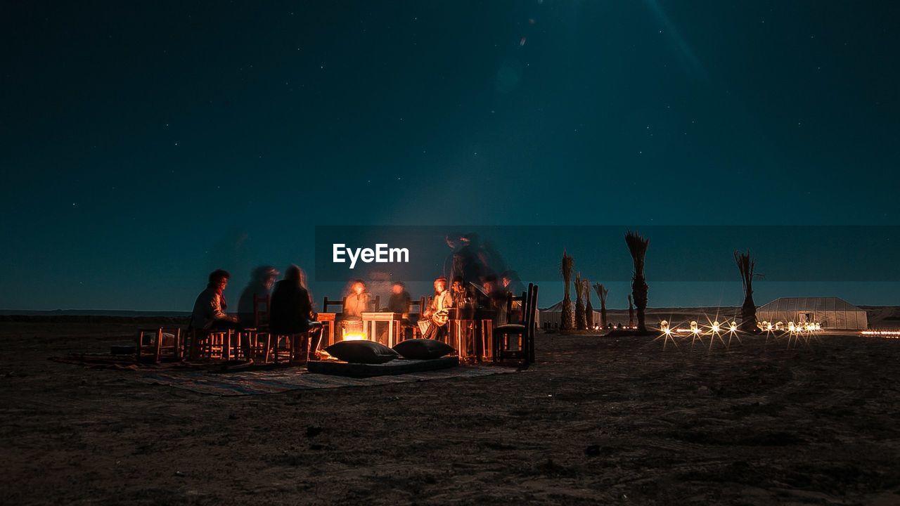 People by bonfire at beach against sky during night