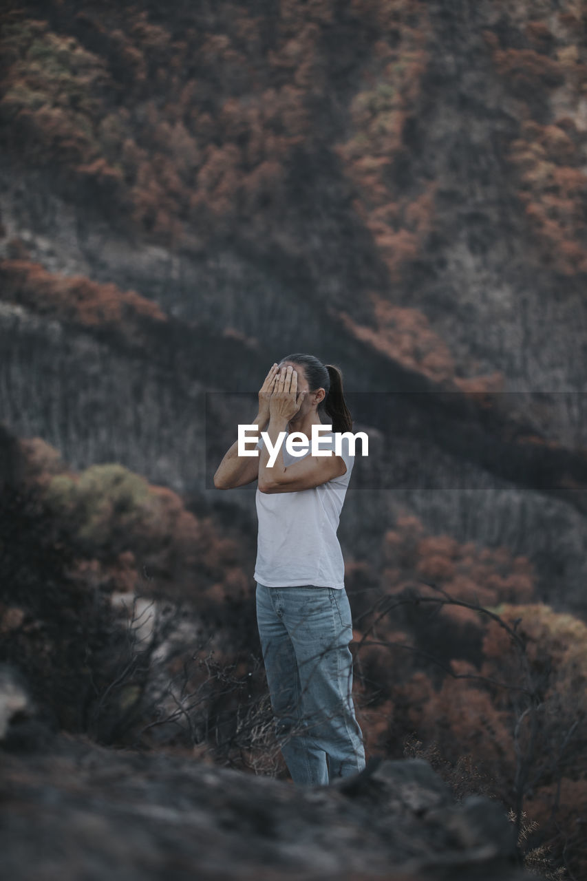 Desperate woman covering face standing in forest