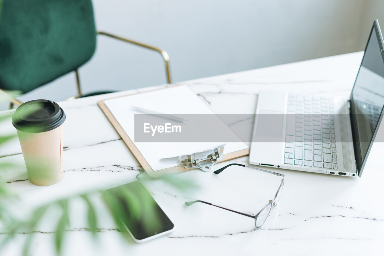 Working place with paper cup of coffee, notes, open laptop, eye glasses and smartphone on table 