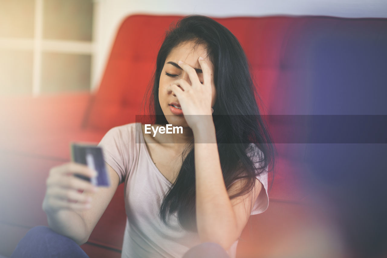 MIDSECTION OF WOMAN USING MOBILE PHONE WHILE SITTING ON LAPTOP