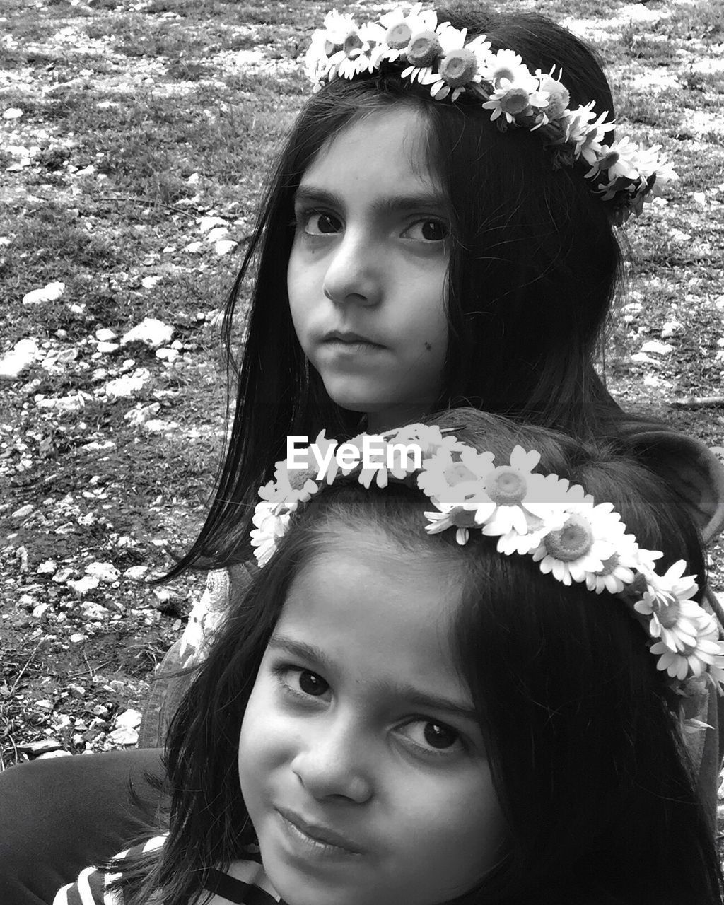 Close-up portrait of sisters wearing flowers while sitting on field