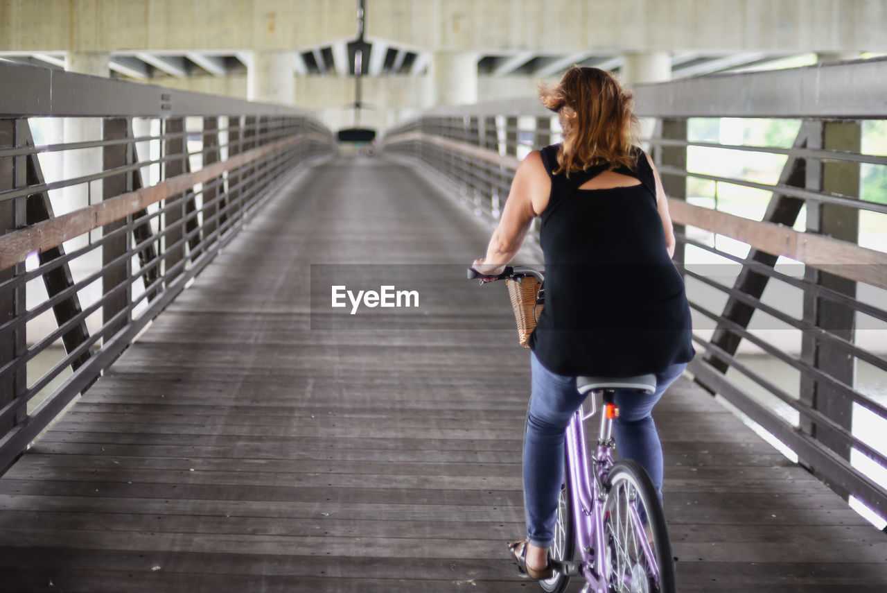 Rear view of woman riding bicycle on bridge