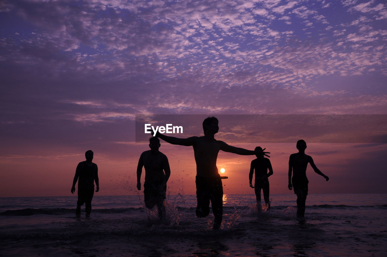 Silhouette people on beach against sky during sunset