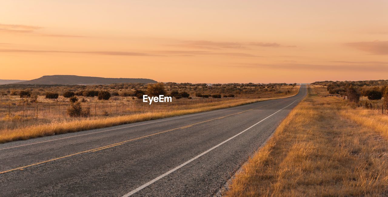 Road by landscape against sky during sunset