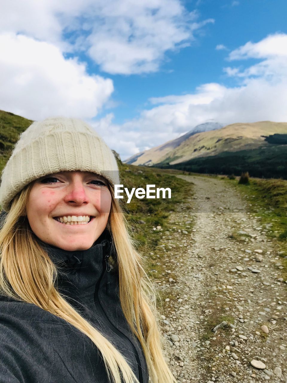 Portrait of smiling woman on dirt road against sky