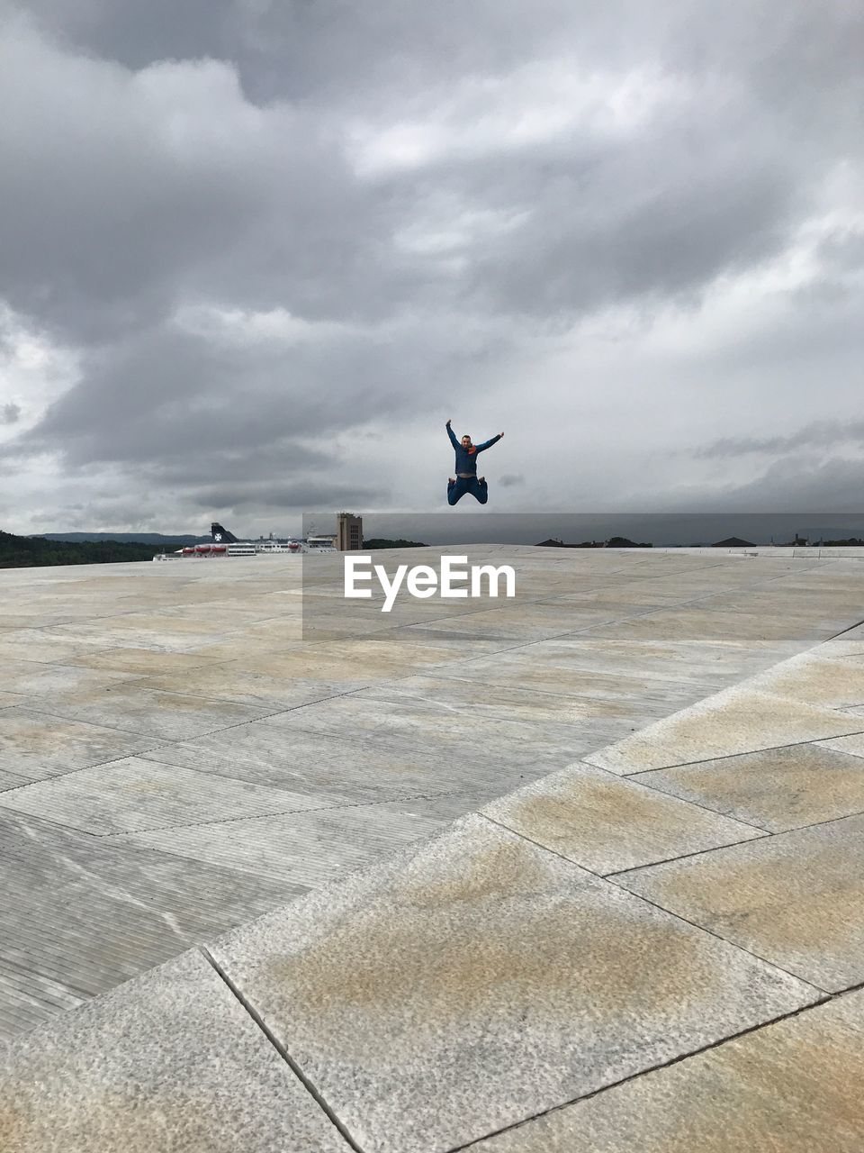 Mid distance view of man jumping on footpath against cloudy sky