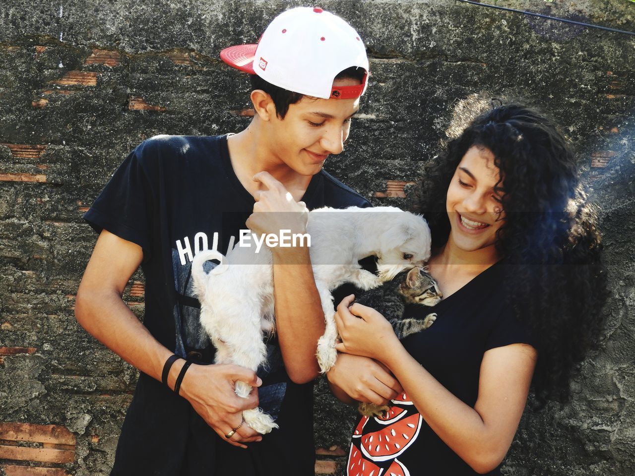 Teenage couple with dog and kitten standing against wall