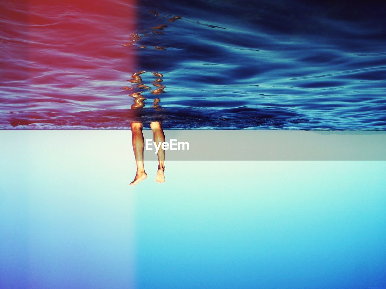 Upside down image of human legs in sea against blue sky