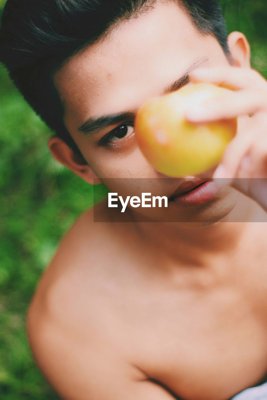 Close-up portrait of shirtless man holding fruit