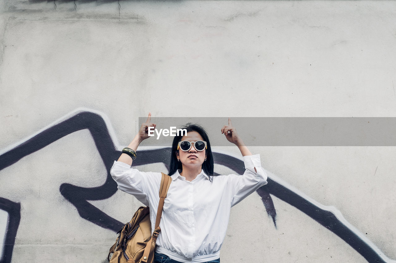 Portrait of woman gesturing while standing against graffiti wall