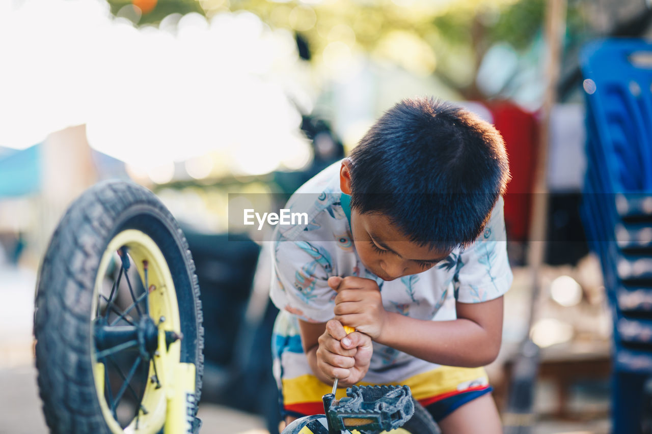 Boy repairing bicycle while standing outdoors