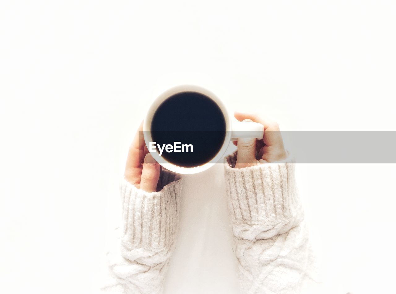 Close-up of hands holding coffee cup over white background