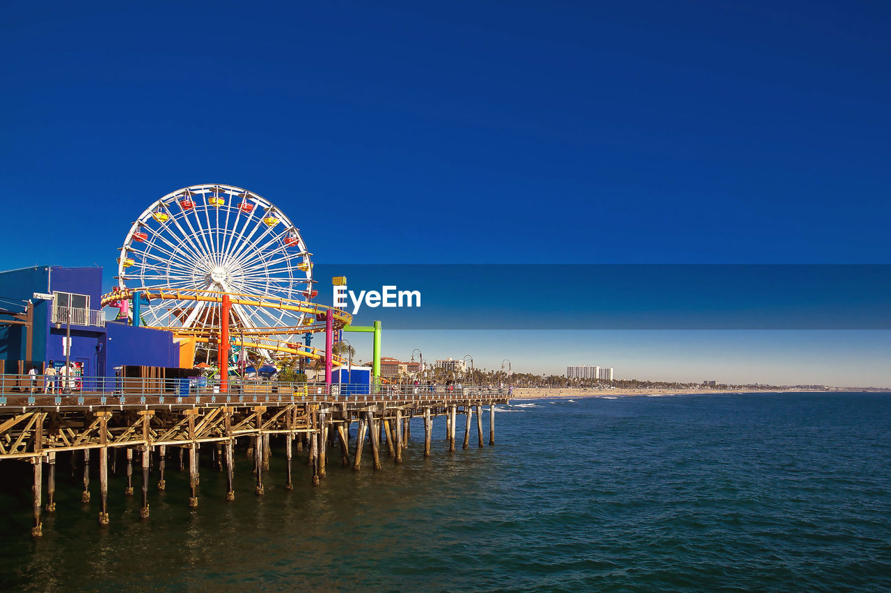 Ferris wheel at beach against clear blue sky