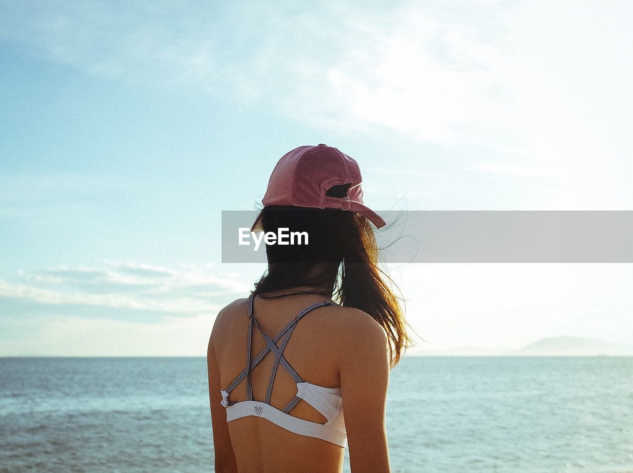 REAR VIEW OF WOMAN STANDING ON BEACH AGAINST SKY