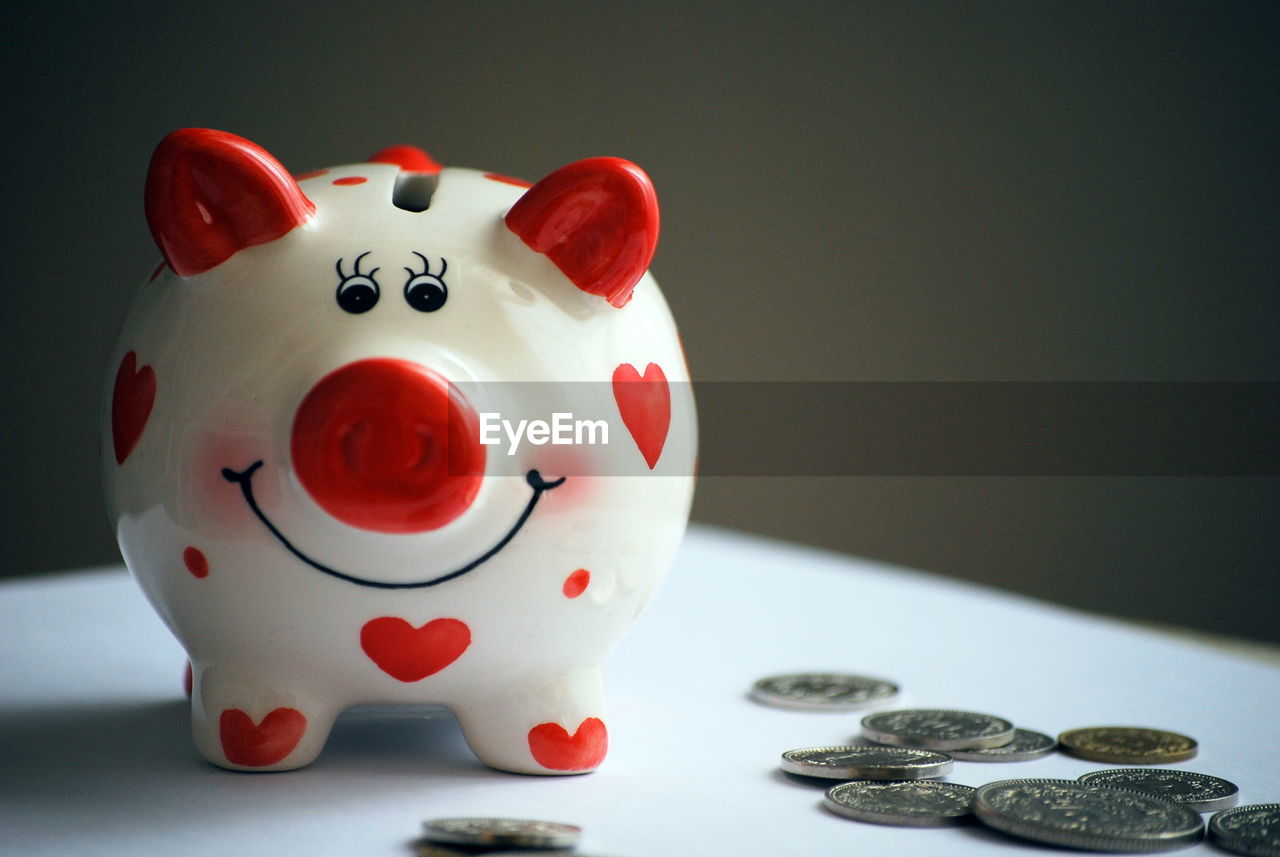 Close-up of coins with piggy bank on table against wall