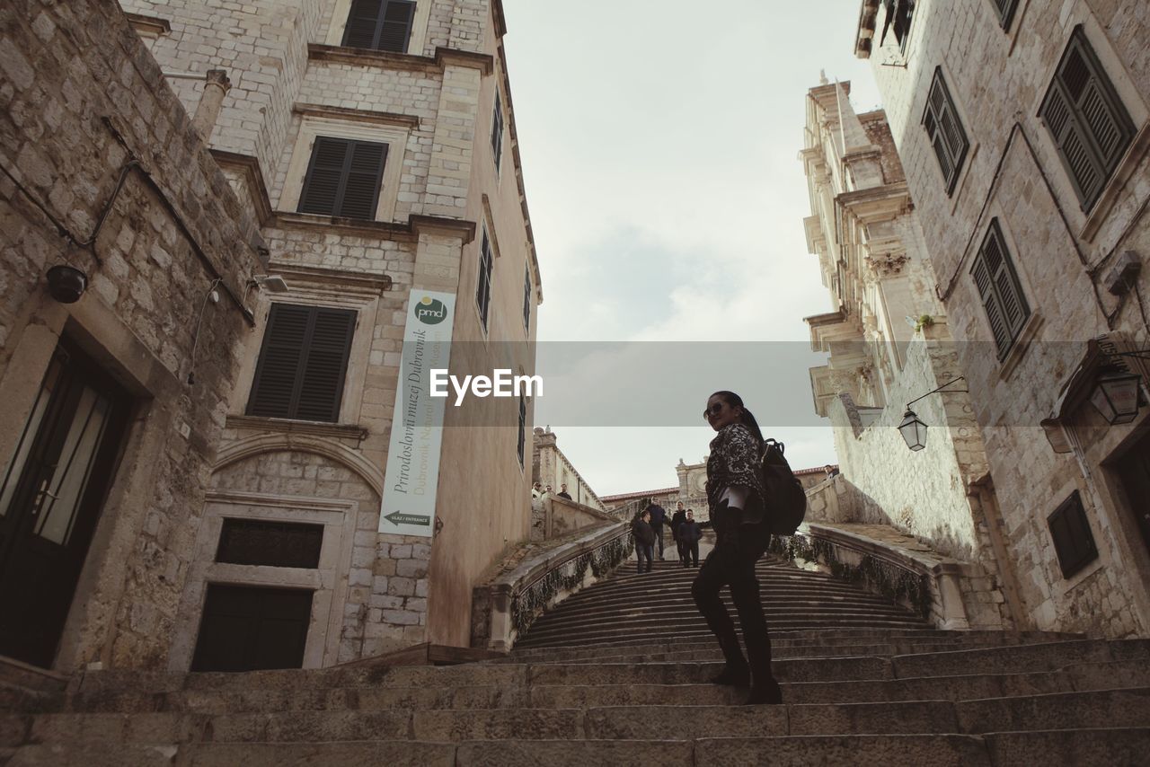 Low angle view of woman walking on staircase amidst buildings