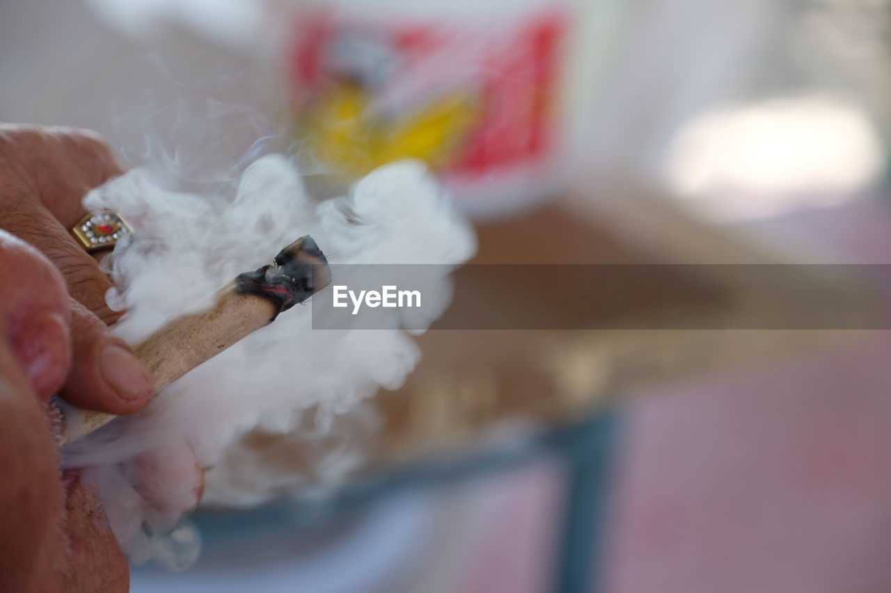 CLOSE-UP OF HAND HOLDING CIGARETTE OUTDOORS