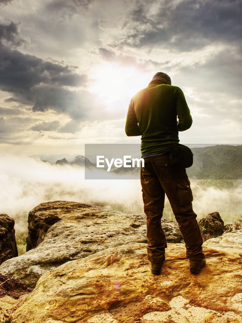 Landscape photograper with camera ready in hand. man on exposed rock takes fall photos with camera