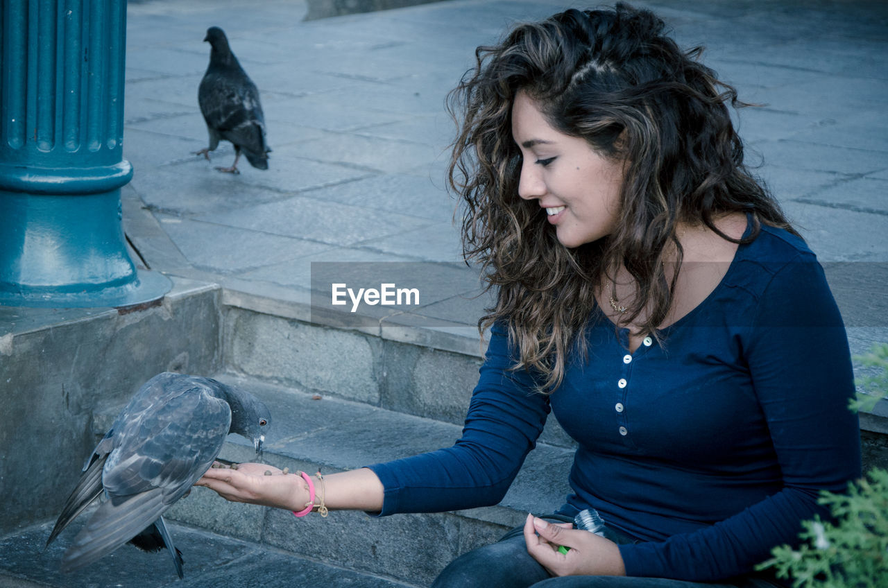 Young woman feeding pigeons while sitting on steps