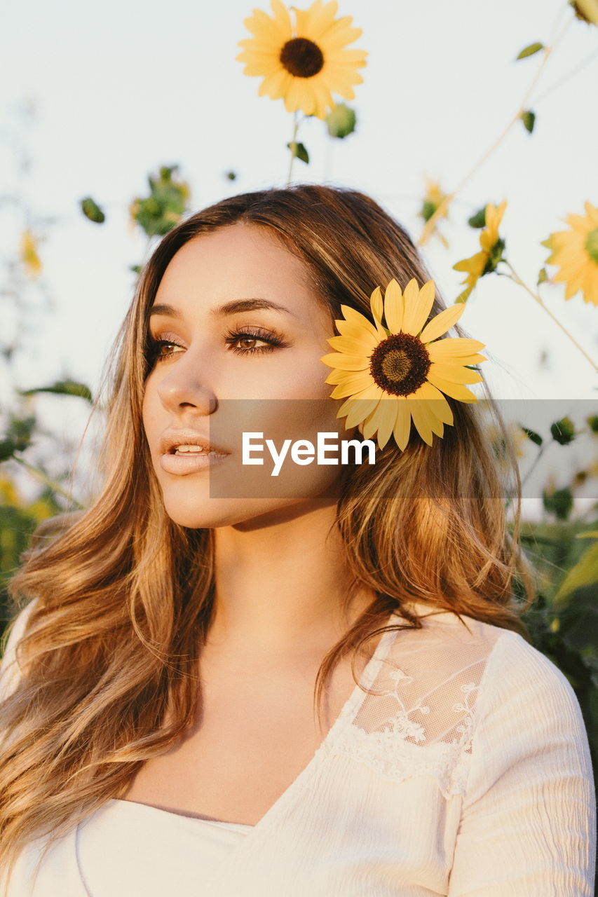 Close-up of beautiful young woman wearing sunflower during sunset