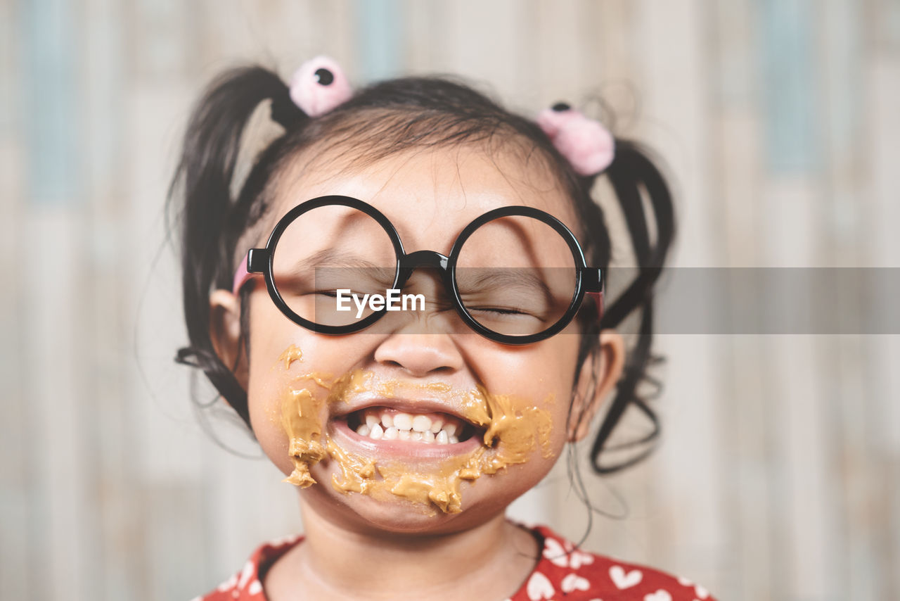 Close-up of cheerful girl eating peanut butter at table against wall