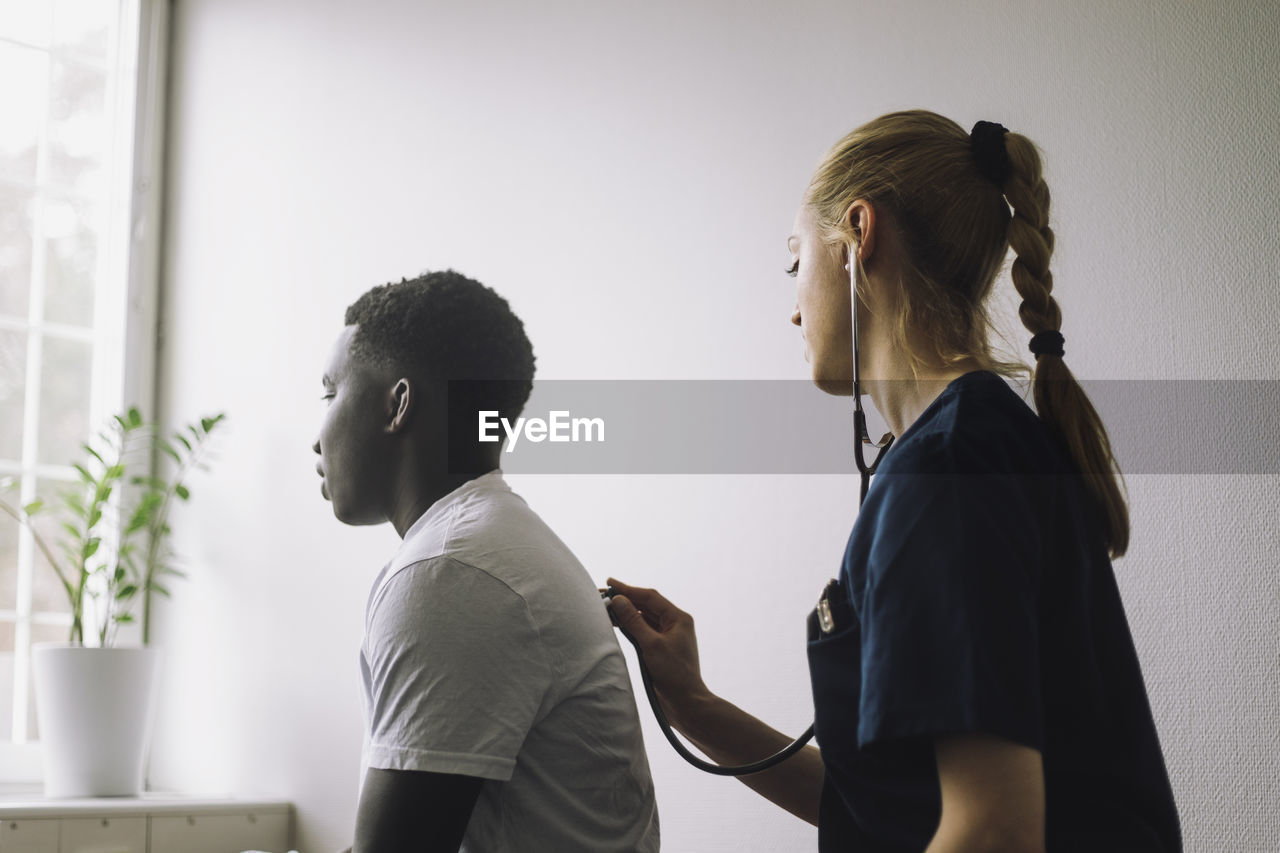 Side view of female nurse examining male teenage patient in clinic