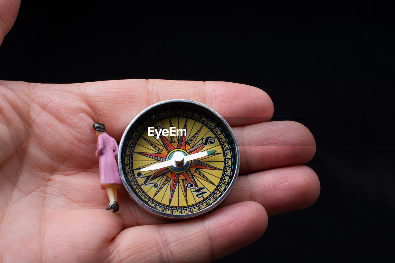 close-up of hand holding navigational compass against black background