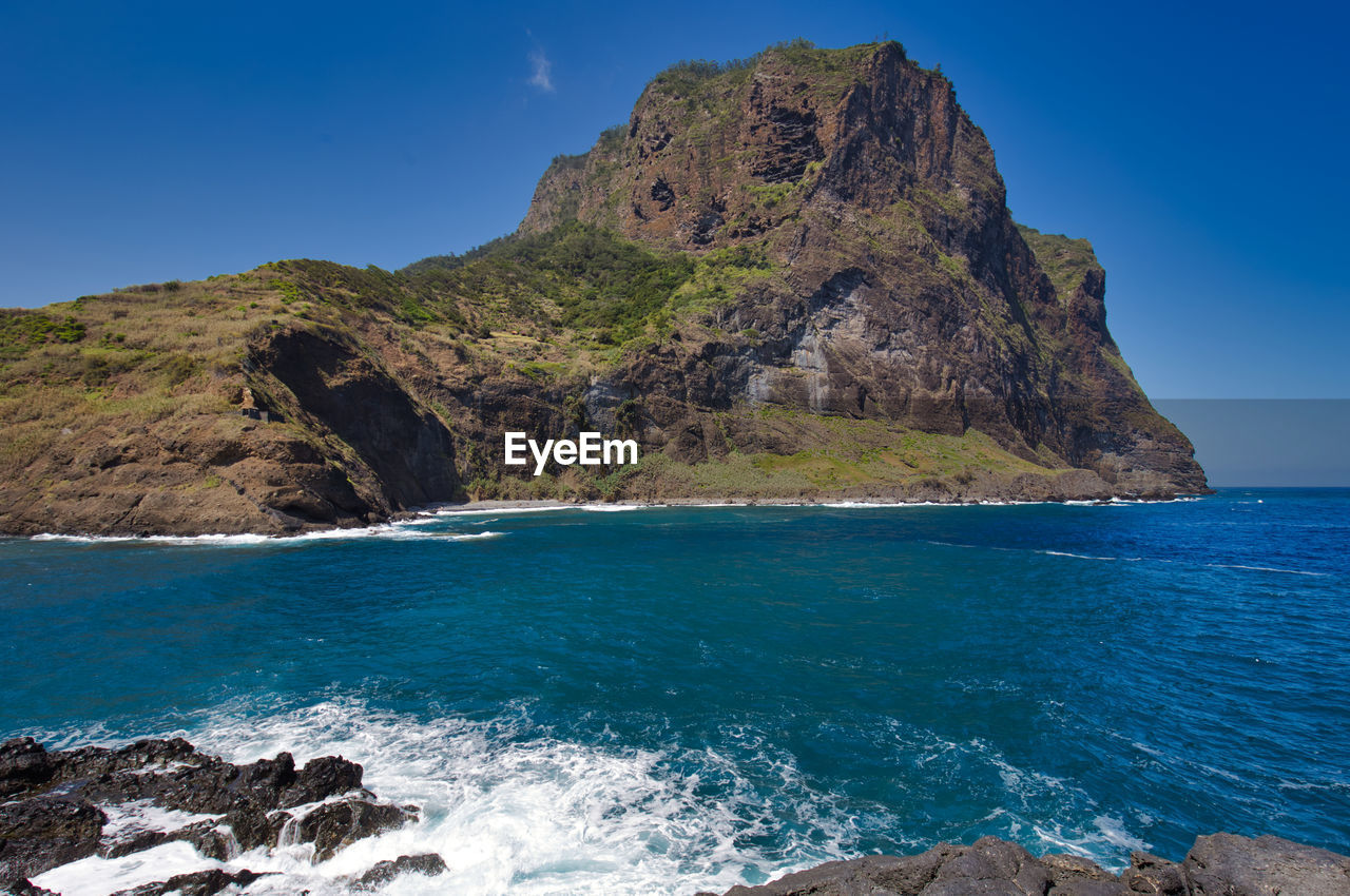 Scenic view of rocks by sea against blue sky