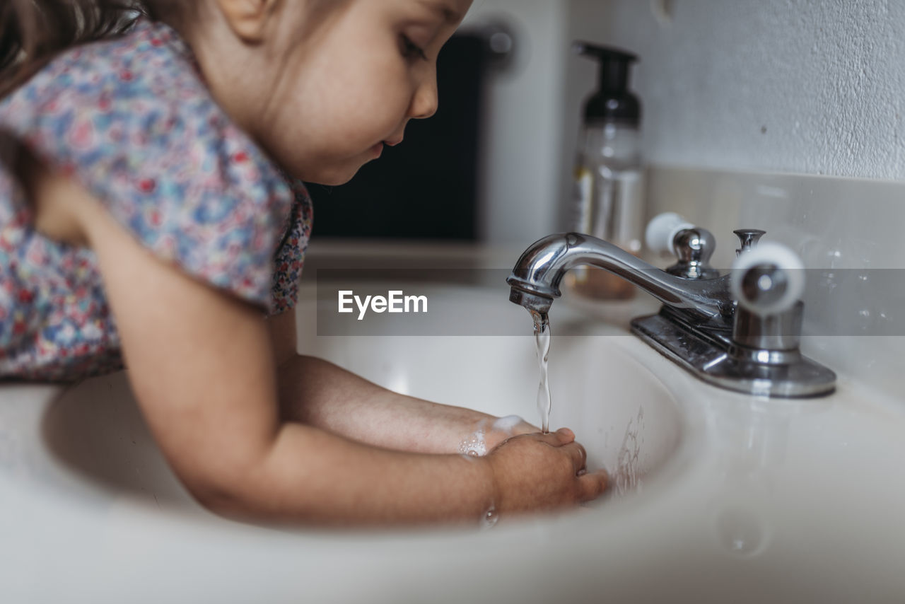 Side view of young girl washing hands in sink with soap