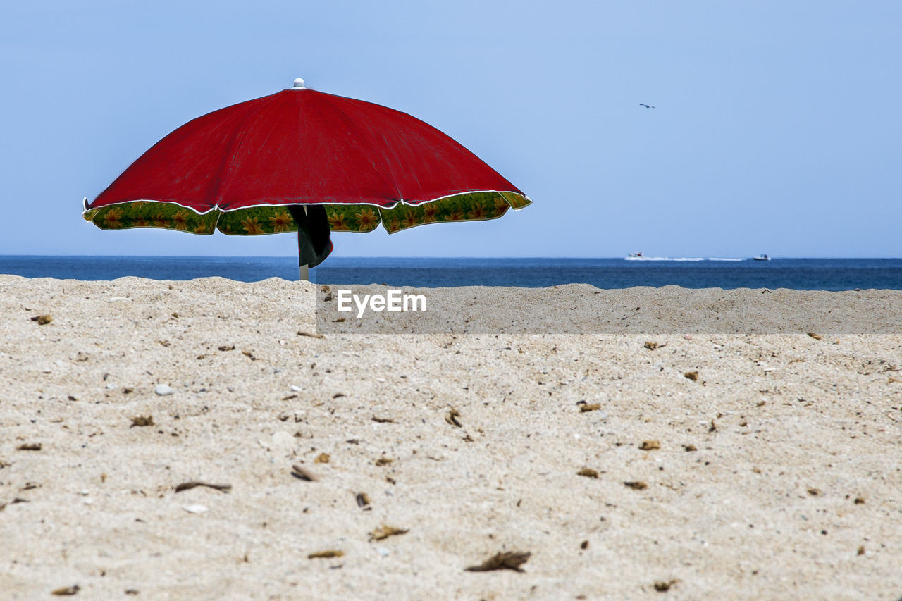 Red umbrella on beach against clear sky