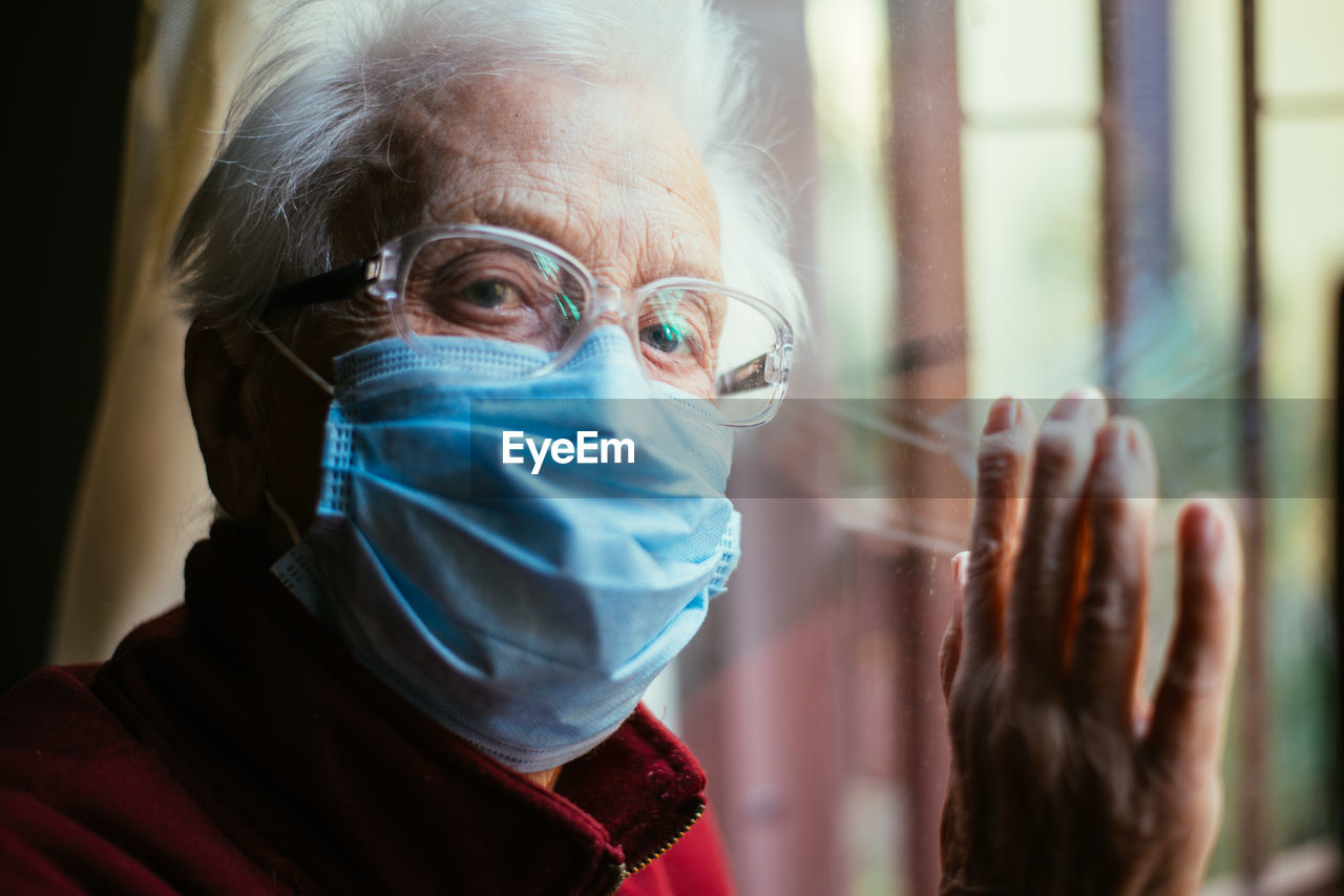 Close-up portrait of senior woman wearing mask with reflection on window