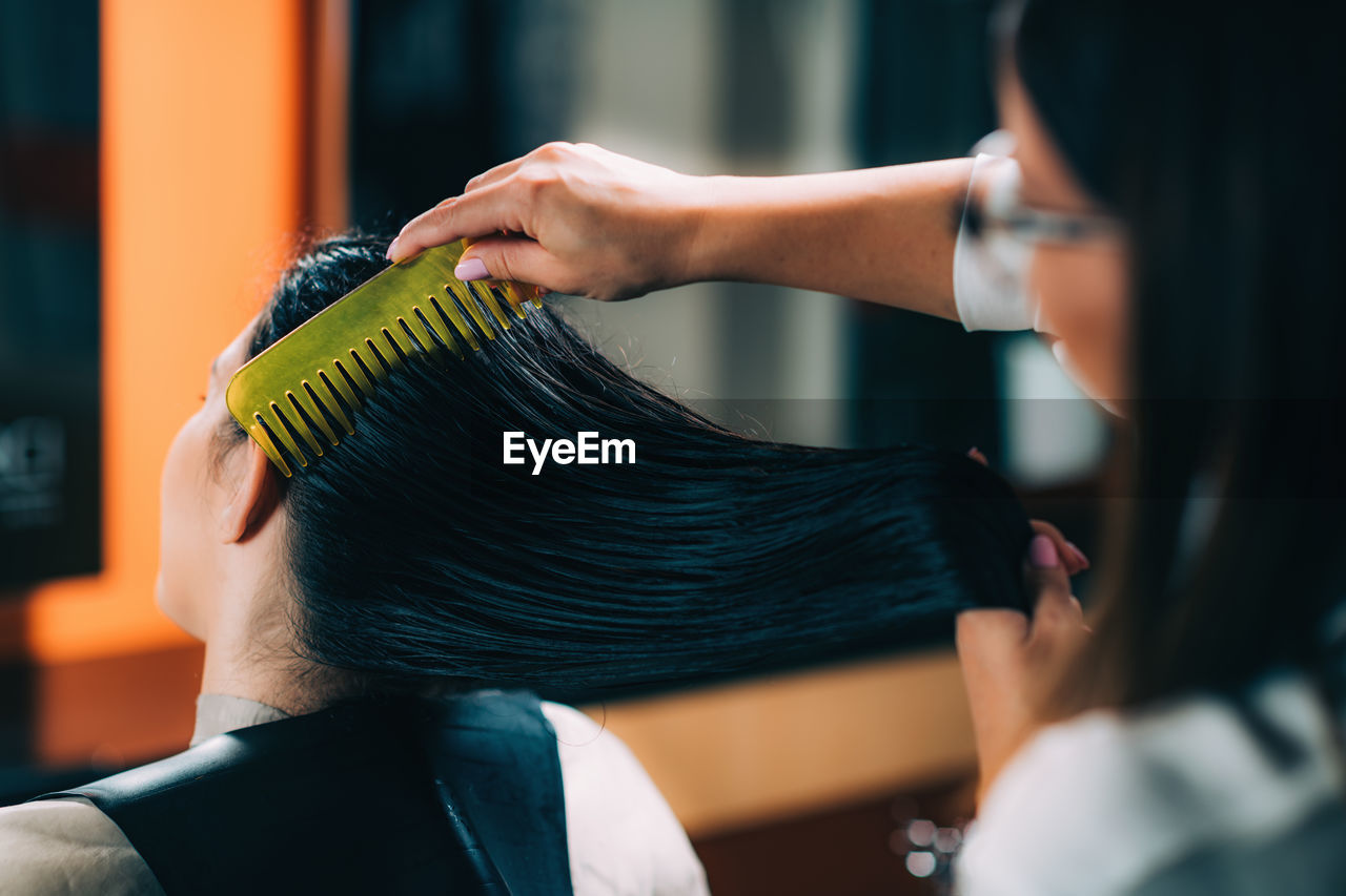 Hairdresser combing customer hair in salon