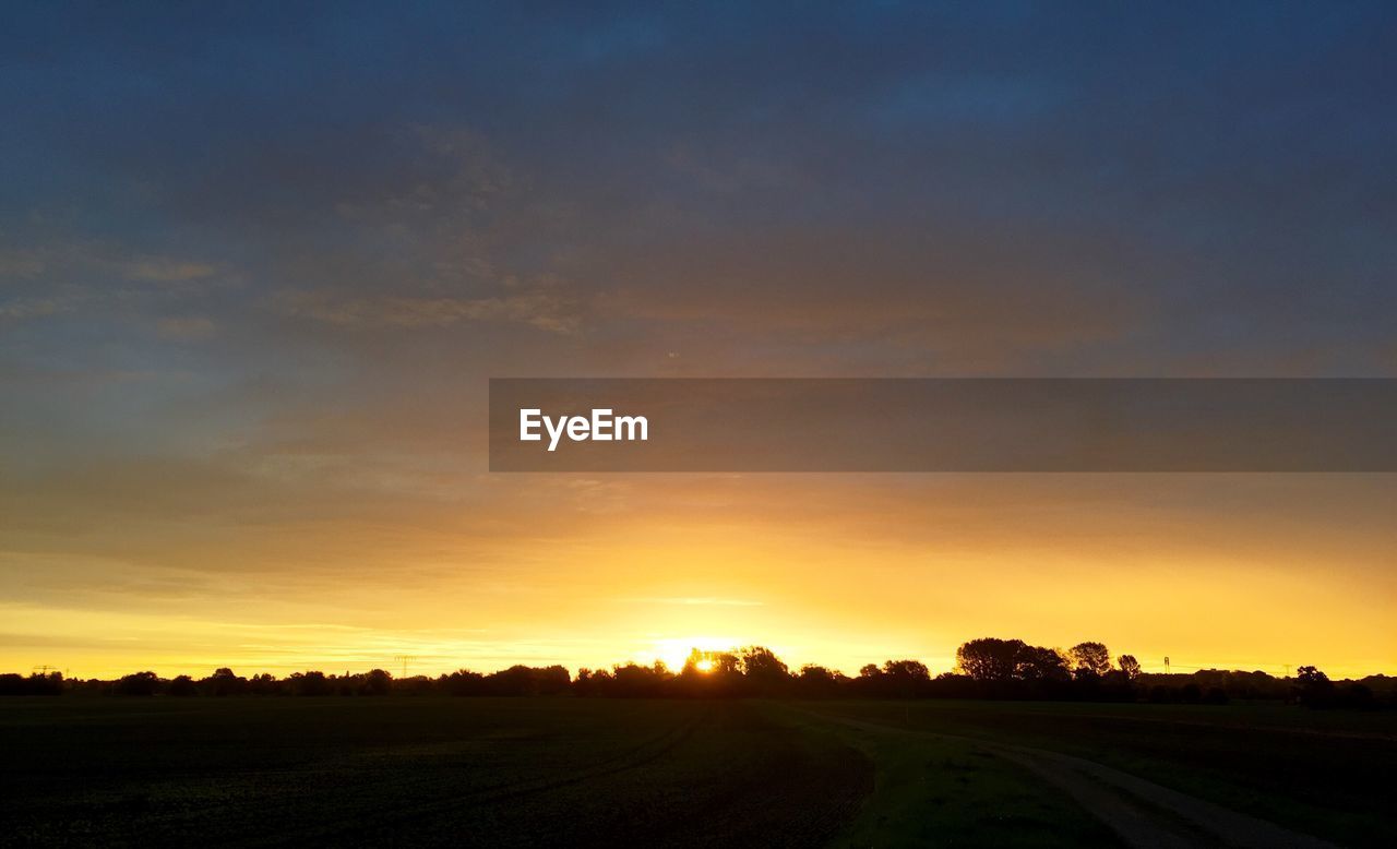 SCENIC VIEW OF SILHOUETTE FIELD AGAINST SKY AT SUNSET