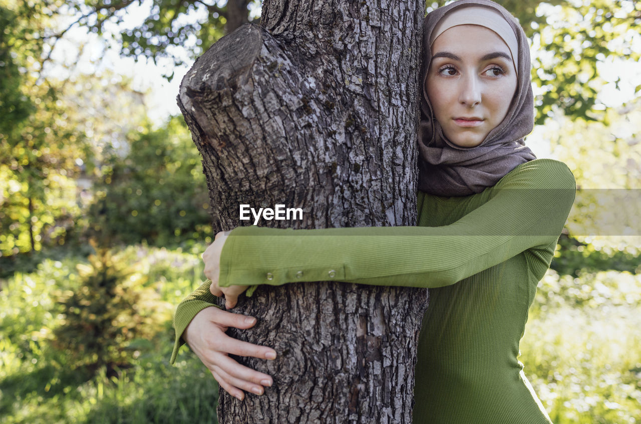 portrait of young woman standing by tree trunk