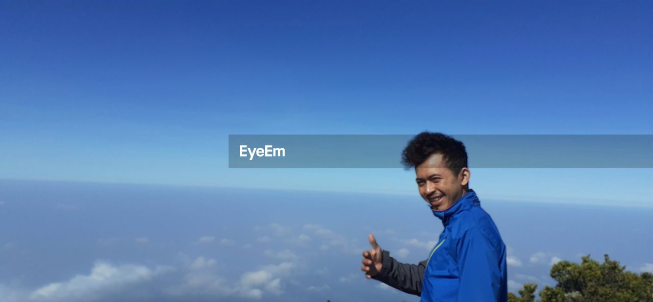 Portrait of smiling man standing against cloudscape