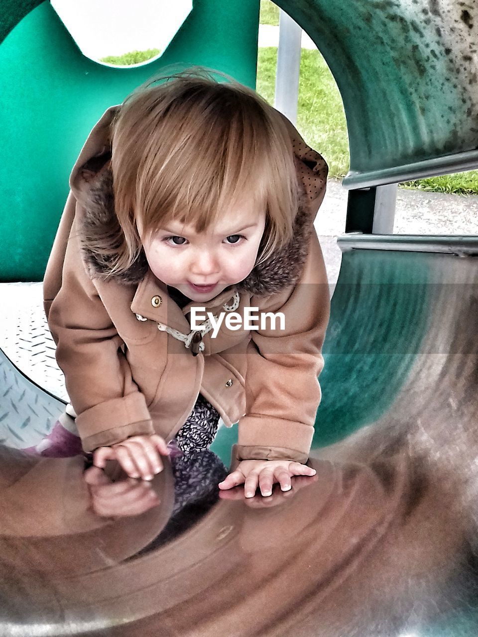 Girl looking away while climbing in tunnel slide at playground