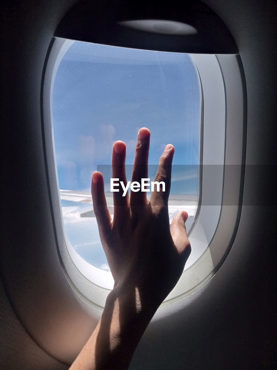Cropped image of airplane flying against sky seen through window