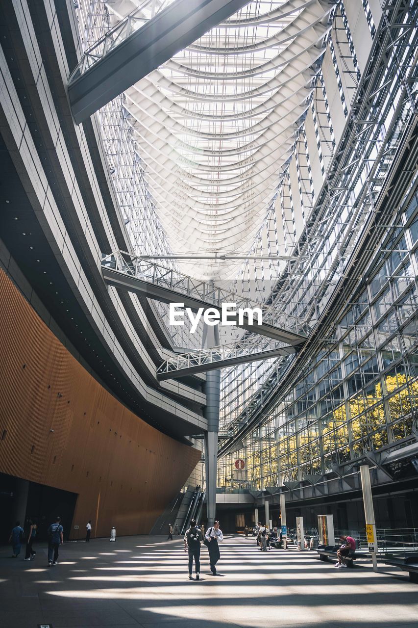 architecture, built structure, city, transportation, group of people, travel, indoors, walking, city life, ceiling, sport venue, adult, travel destinations, mode of transportation, building, day, large group of people, infrastructure, men, sunlight, stadium, headquarters, crowd, facade, futuristic, business, arena, airport terminal, road, convention center