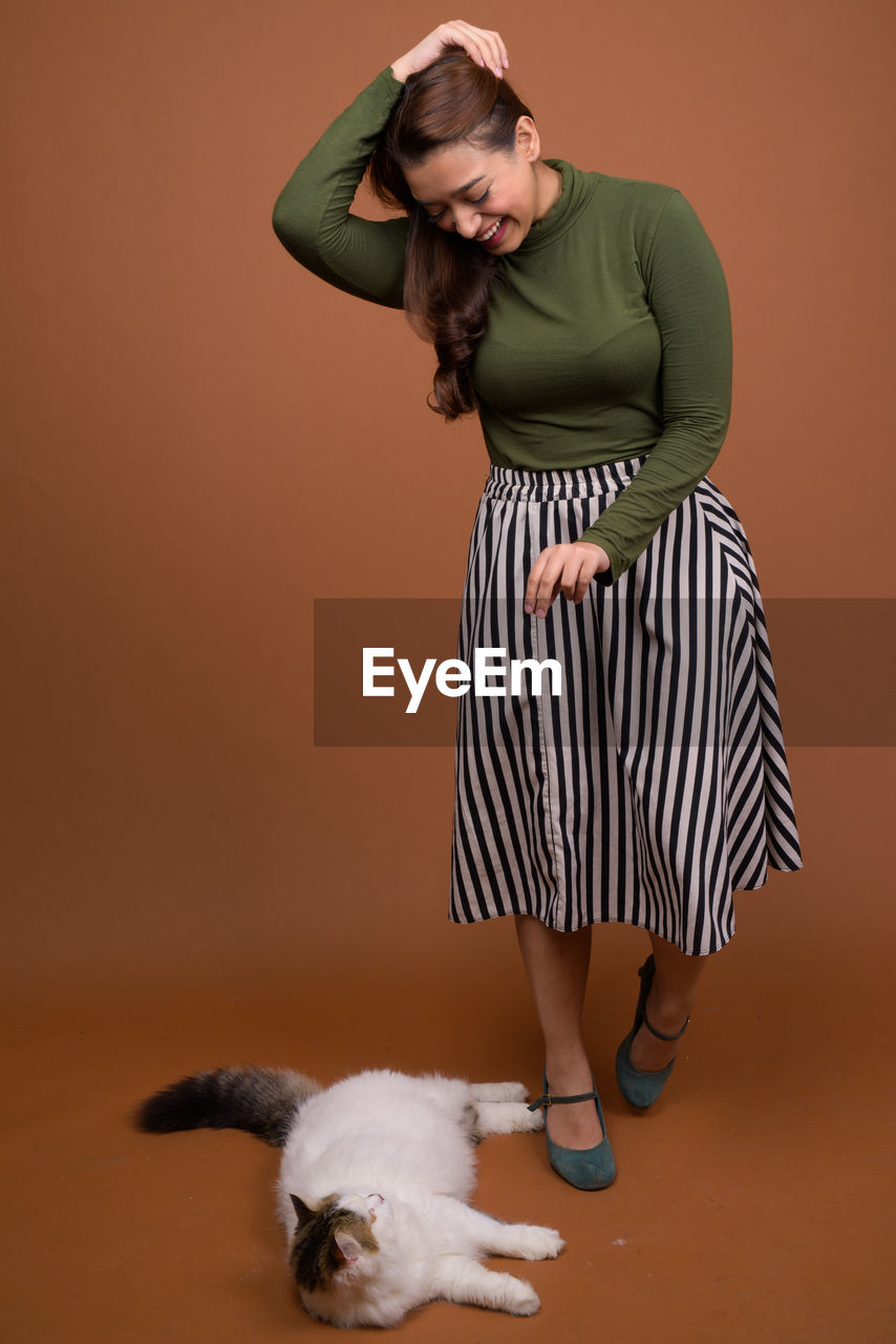 Woman with cat standing against brown background