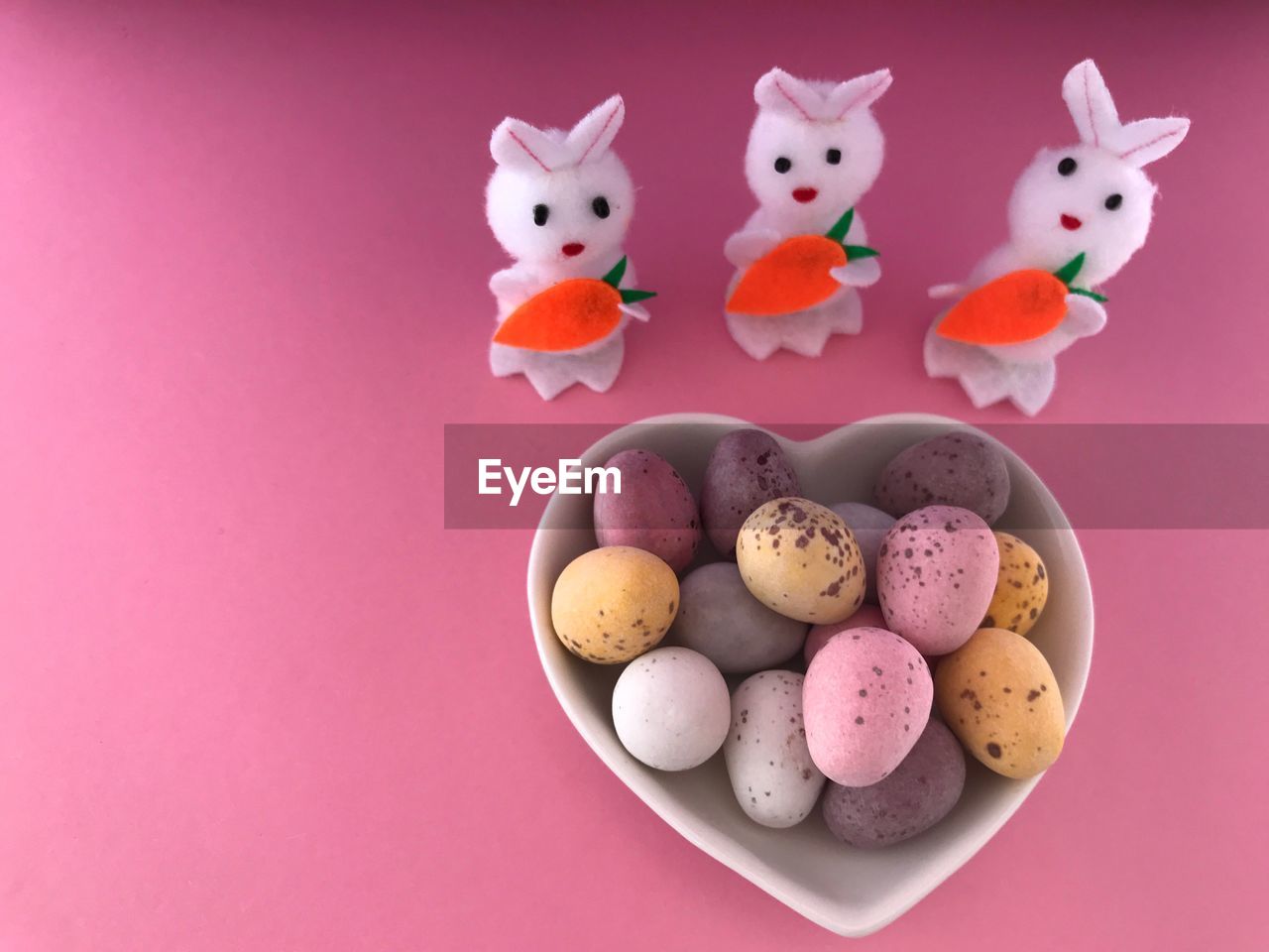 Sugar coated mini chocolate easter eggs in heart shaped dish , and three toy easter rabbits 