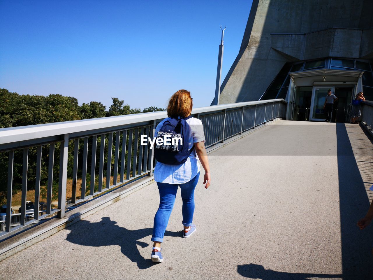 Rear view of woman walking on footbridge against clear sky