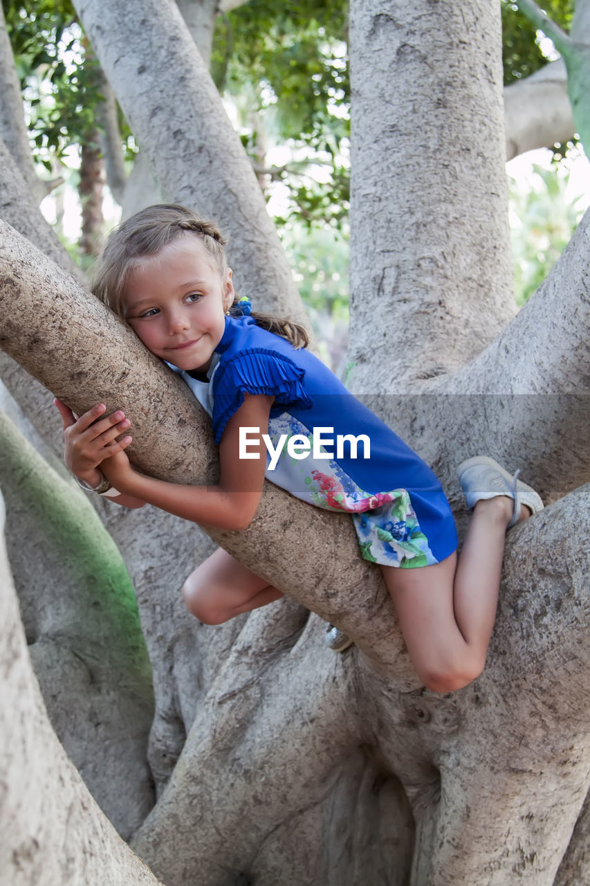 Full length of girl sitting on tree trunk outdoors