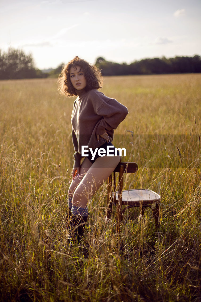  portrait woman in a sweater and shorts sitting on a field with grass on a wood chair in autumn