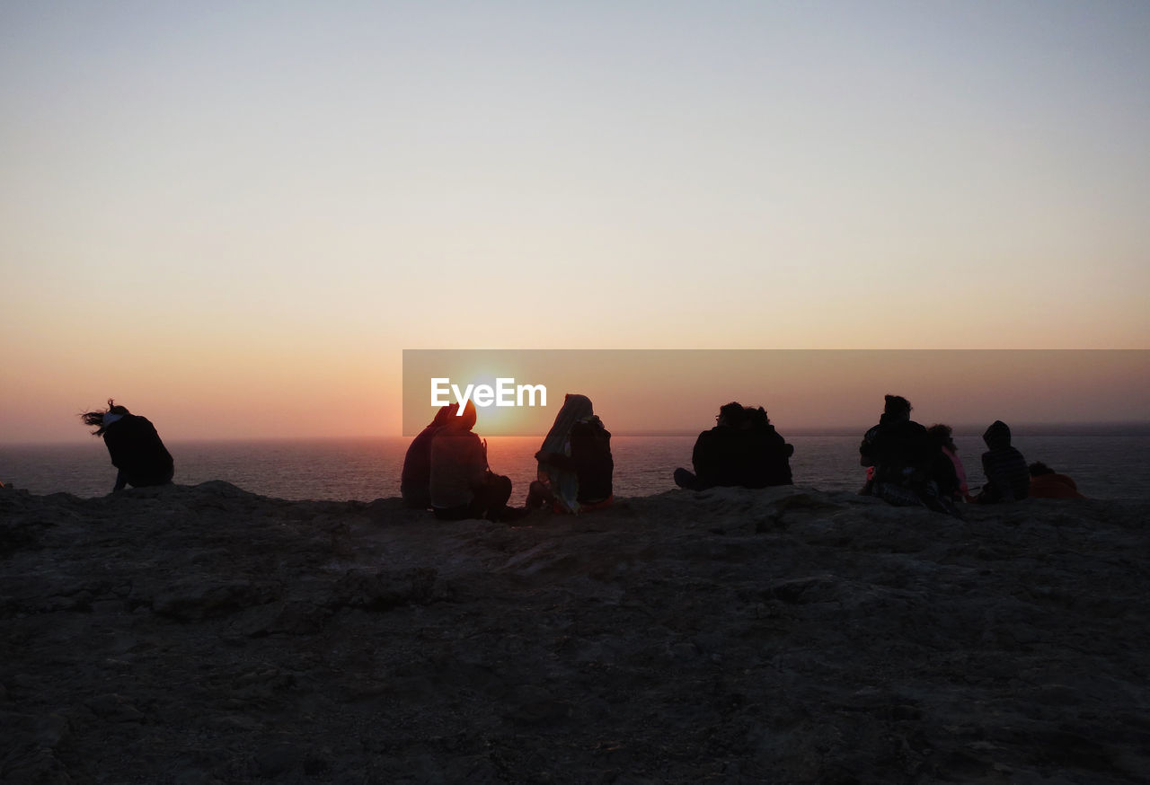 People sitting on rocks against sea during sunset