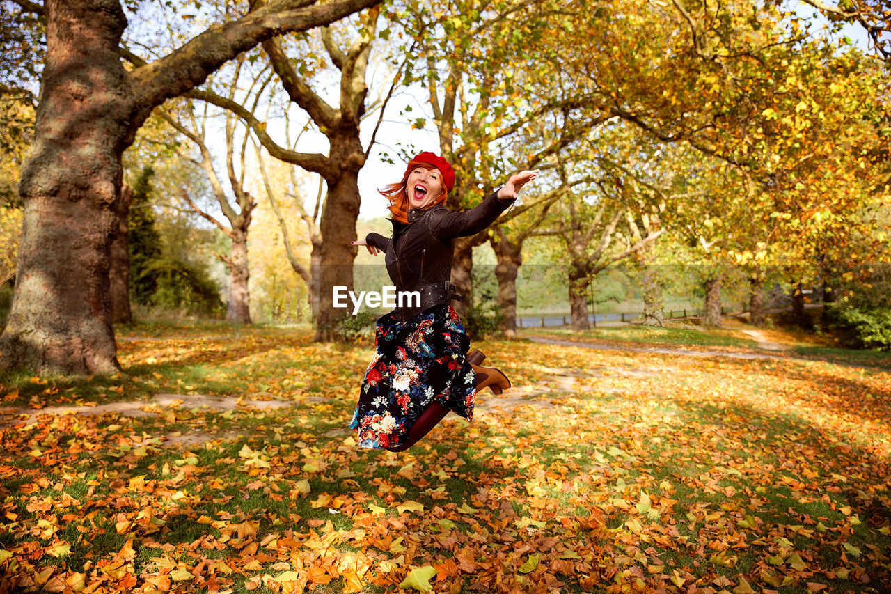 Cheerful woman jumping over field during autumn