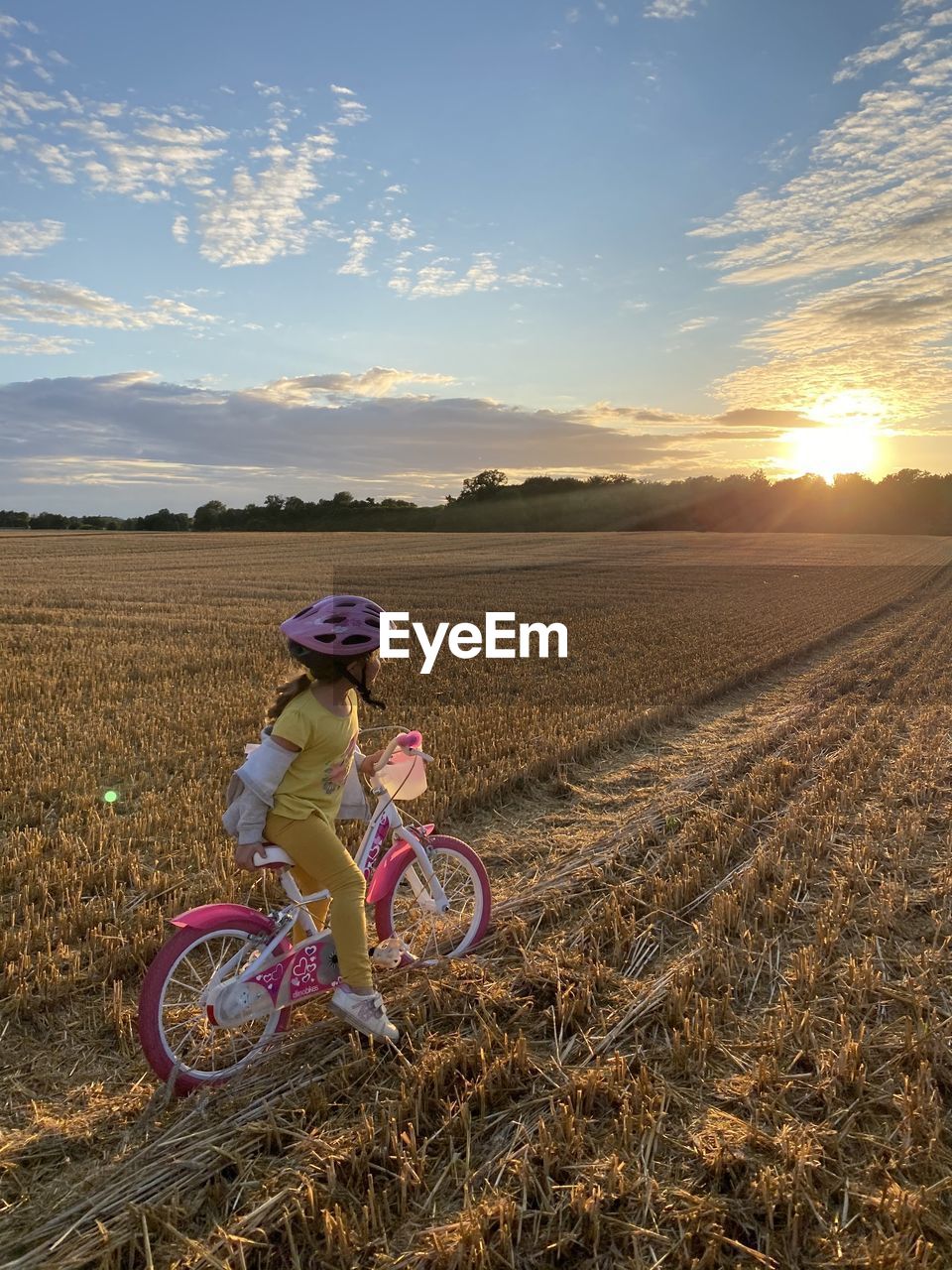 Woman riding bicycle on field against sky during sunset